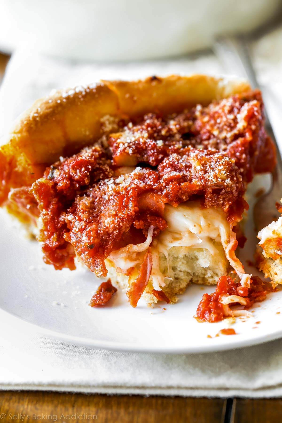 slice of deep dish pizza on a white plate with a fork