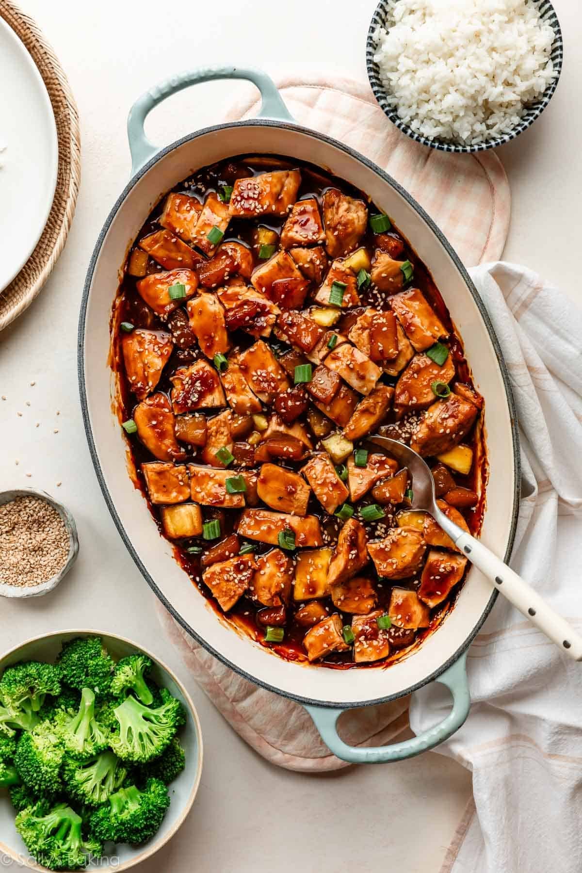 baked pineapple teriyaki chicken in oval baking dish with bowl of white rice and broccoli surrounding it.