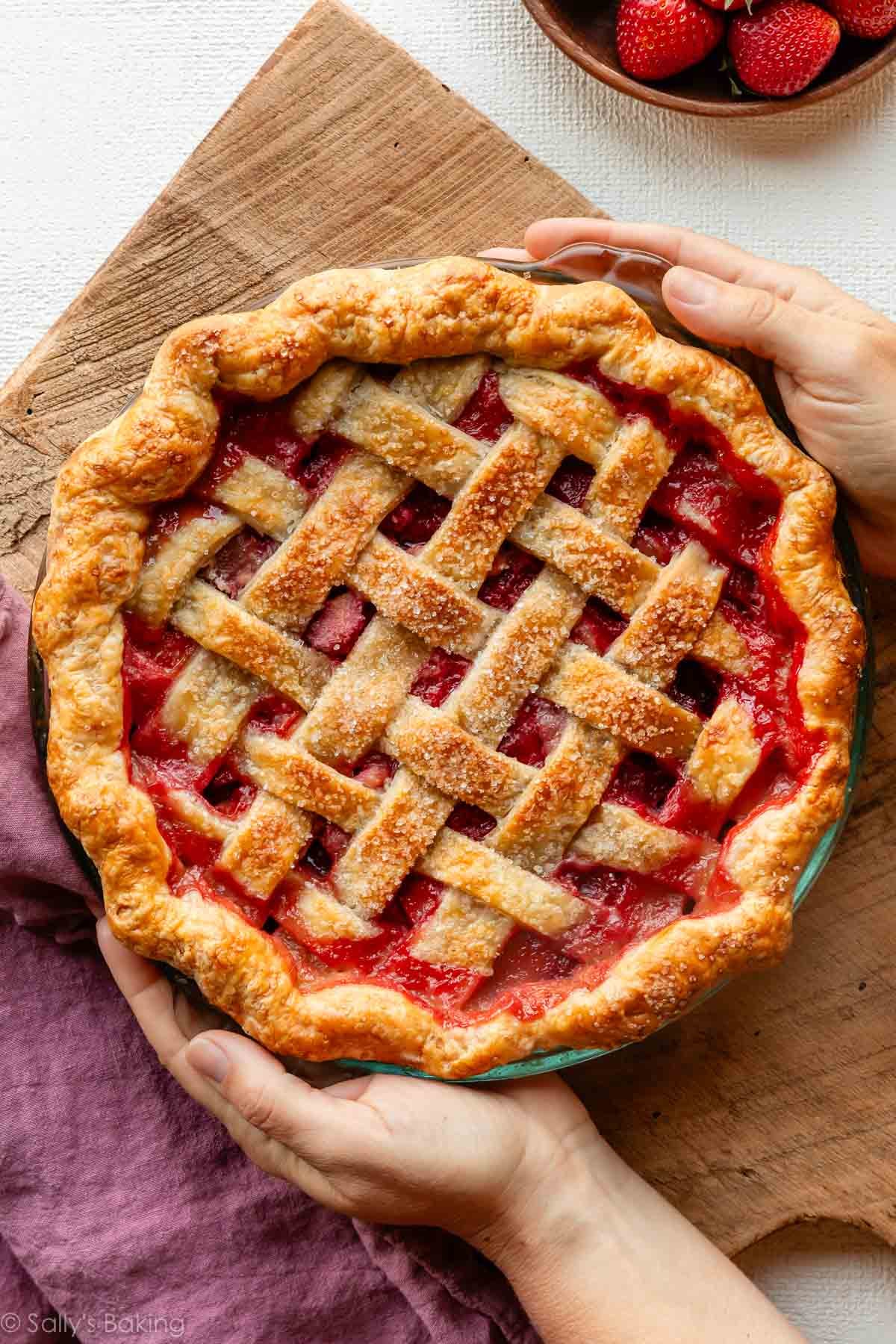 hands holding a lattice crust strawberry rhubarb pie.