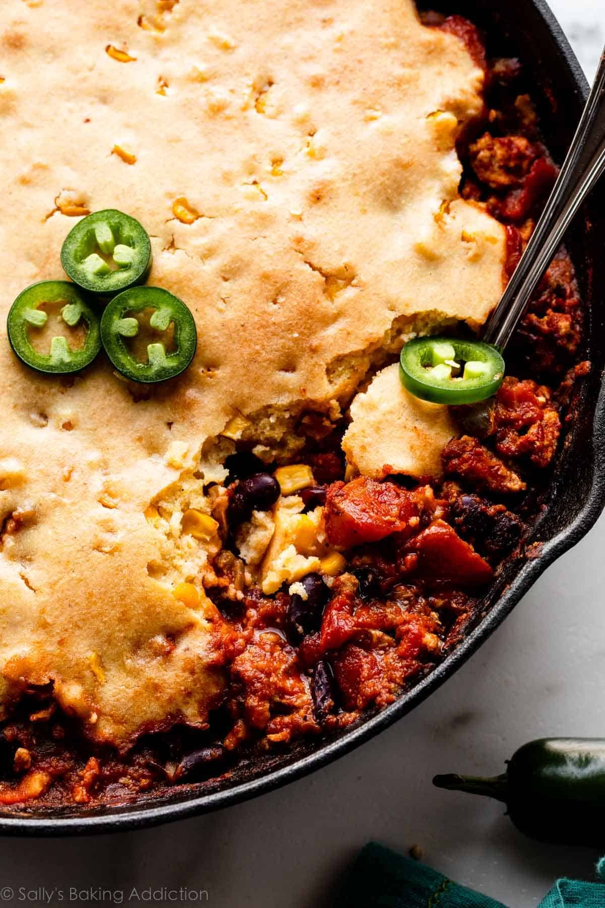 cornbread topped chili casserole in cast iron skillet topped with sliced jalapeño.