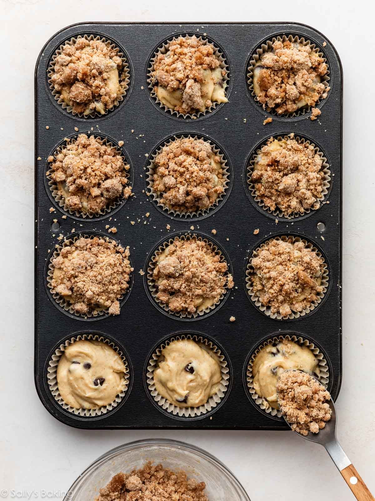 spoon adding crumb topping to chocolate chip muffin batter.