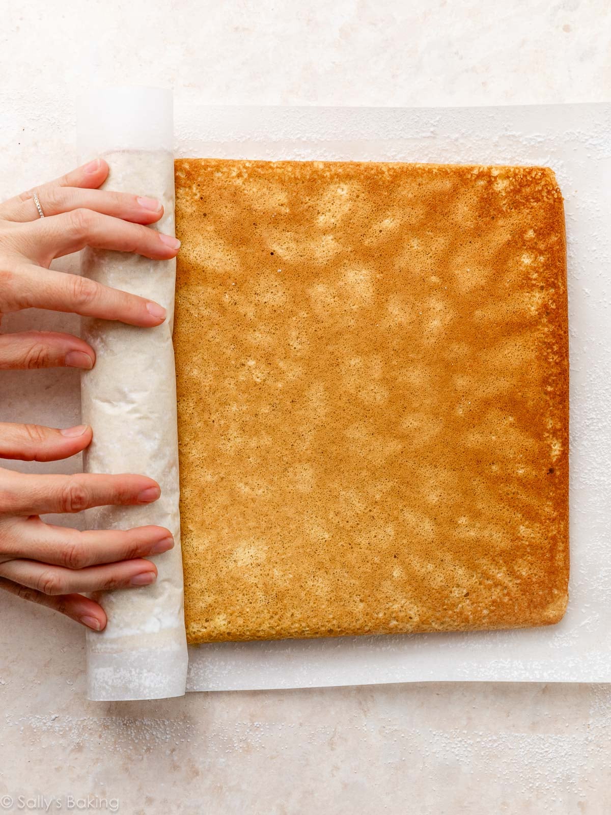 hands rolling up cake roll in parchment paper.