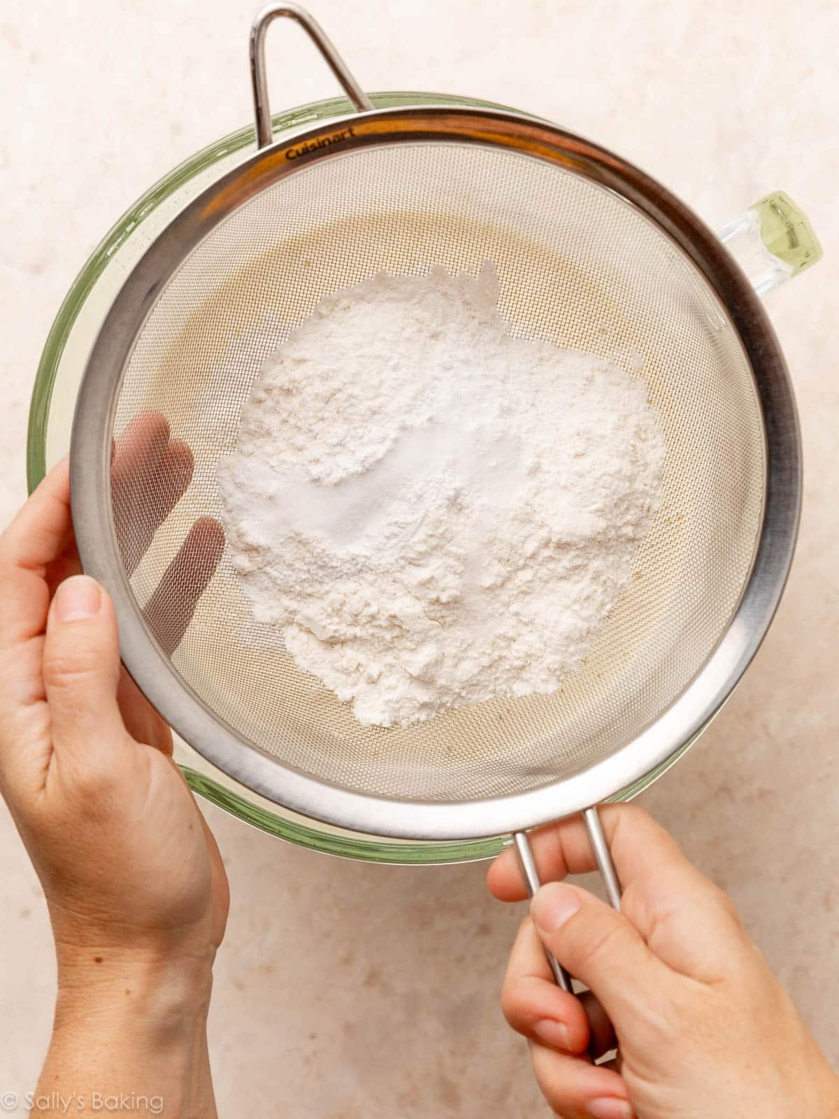 hands holding sieve of dry ingredients over bowl.