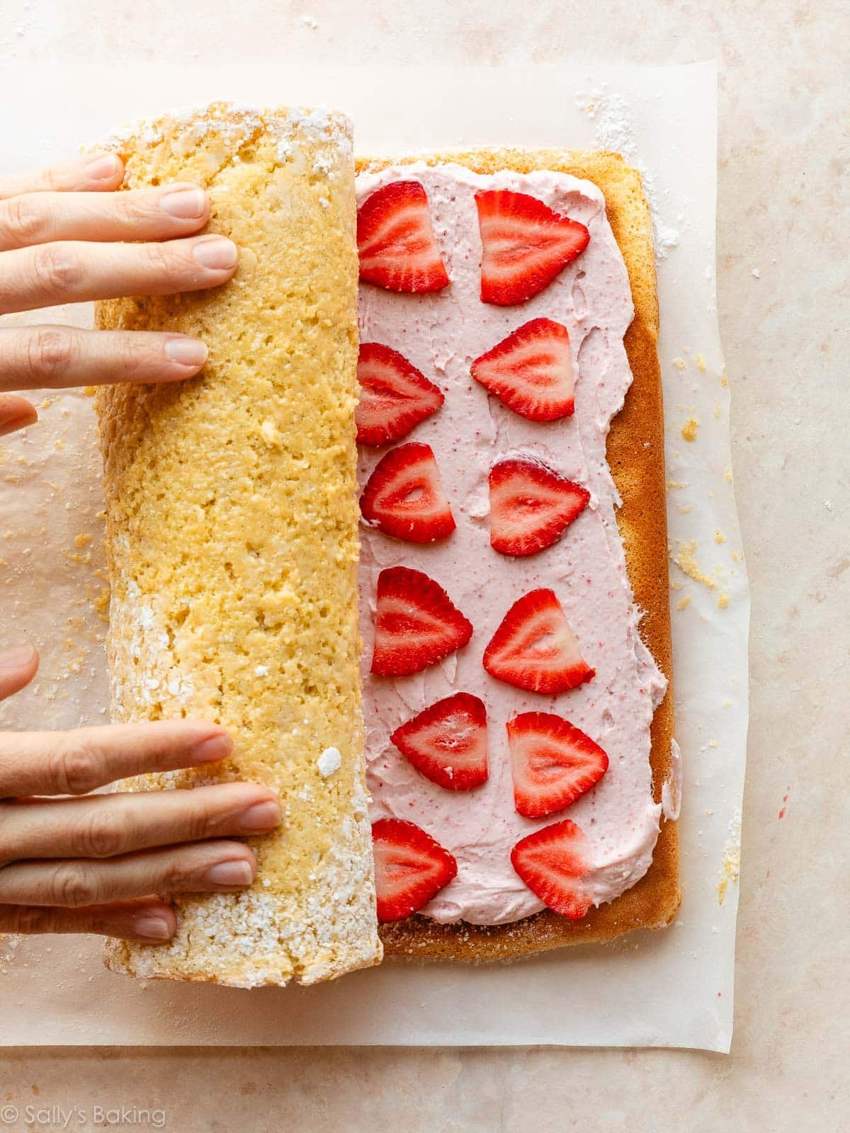 hands rolling up strawberry-lined cake roll.