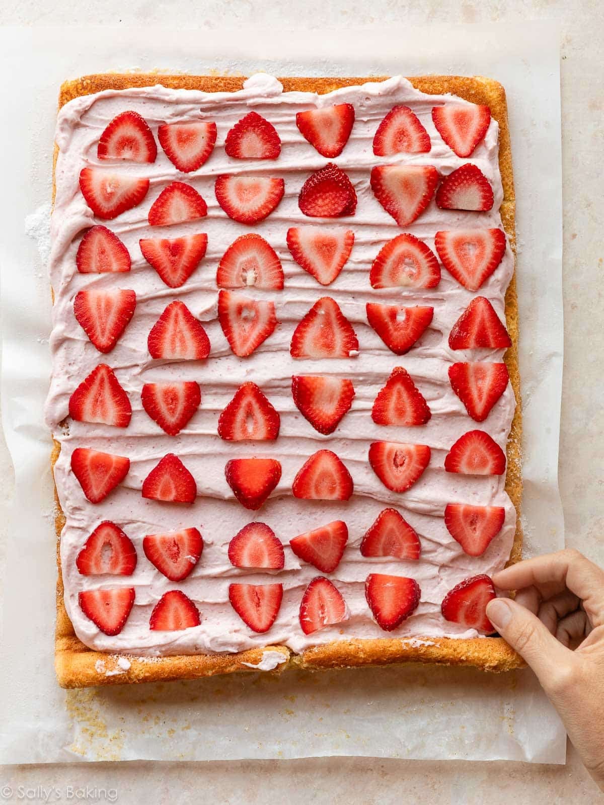 hand adding sliced strawberries on filling.