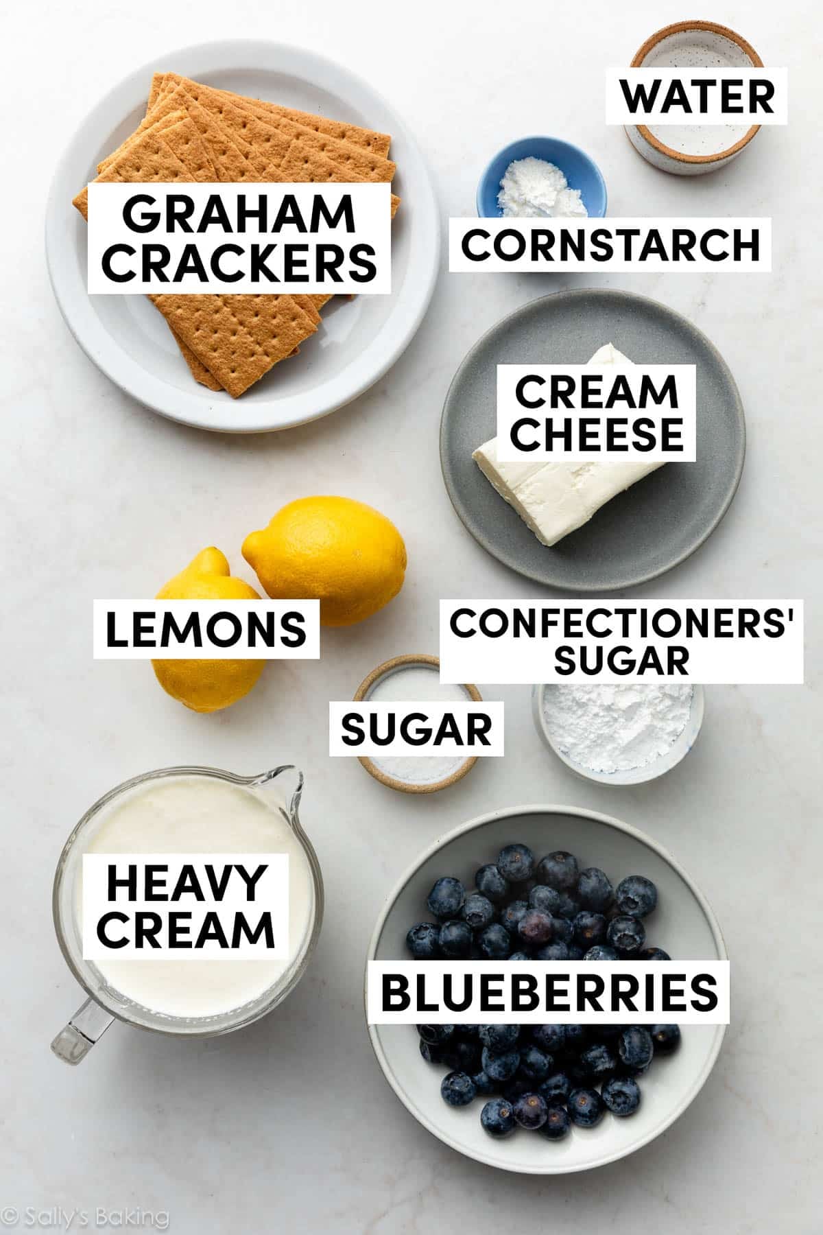 ingredients in bowls including graham crackers, lemons, blueberries, cream cheese, and sugar.