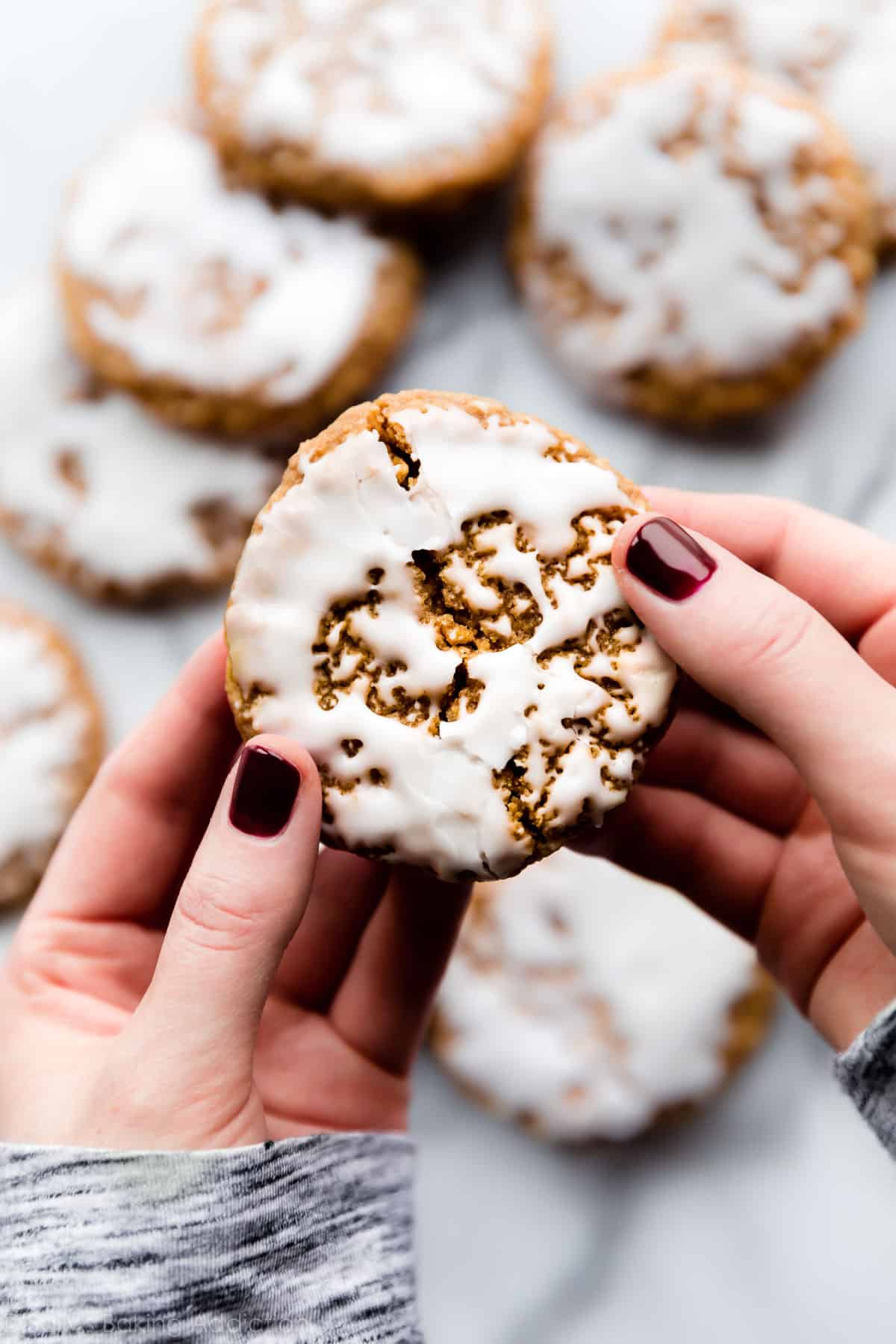 iced oatmeal cookie with hands breaking it in half