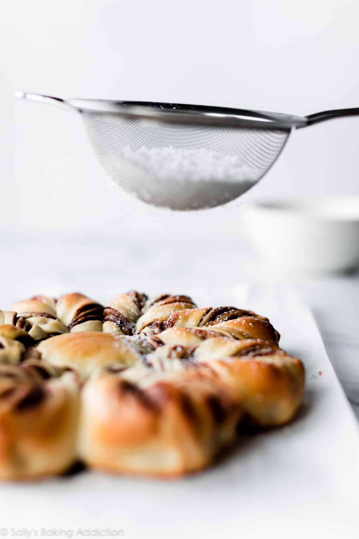 using a metal sieve to add confectioners' sugar on top of cinnamon sugar star bread