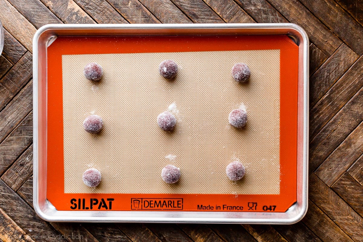red velvet cookie dough balls rolled in sugar arranged on baking sheet