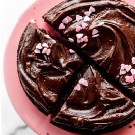overhead photo of chocolate ganache and pink heart sprinkles on a chocolate cake