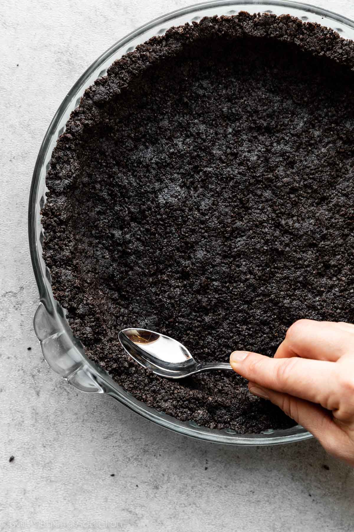 spoon smoothing out edges of chocolate cookie pie crust.