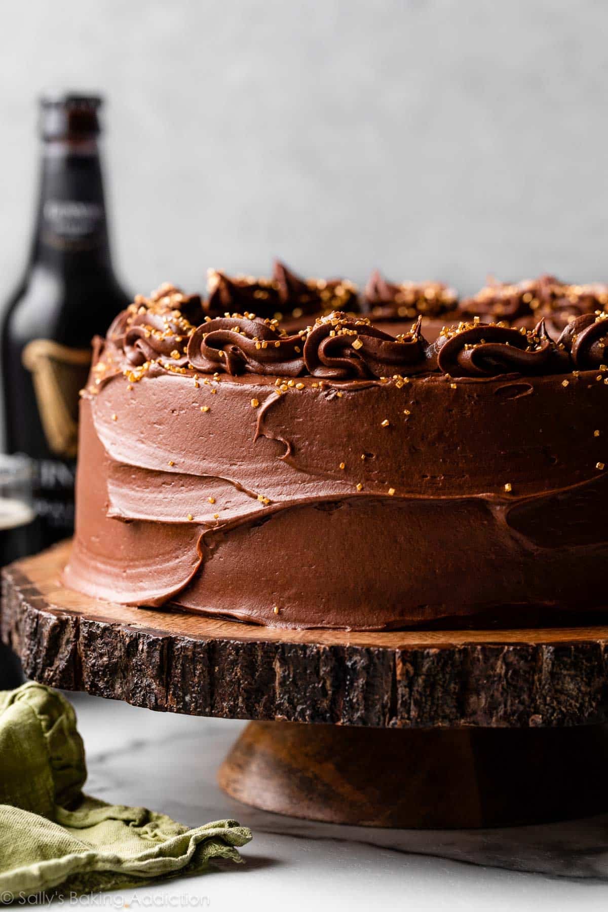 Guinness cake with chocolate frosting and gold sprinkles on wooden cake stand.