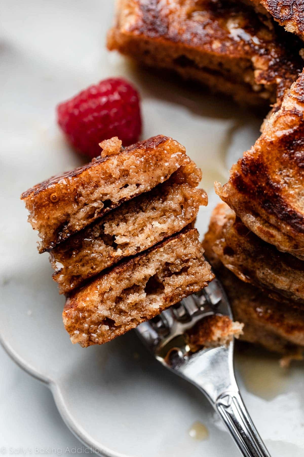 fork sticking through 3 cut-out pieces of whole wheat pancakes with raspberry also on plate.
