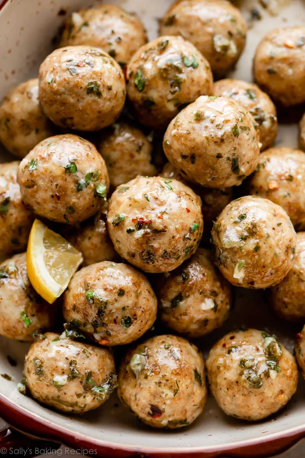 chicken meatballs in a pile topped with lemon butter herb sauce with red pepper flakes.