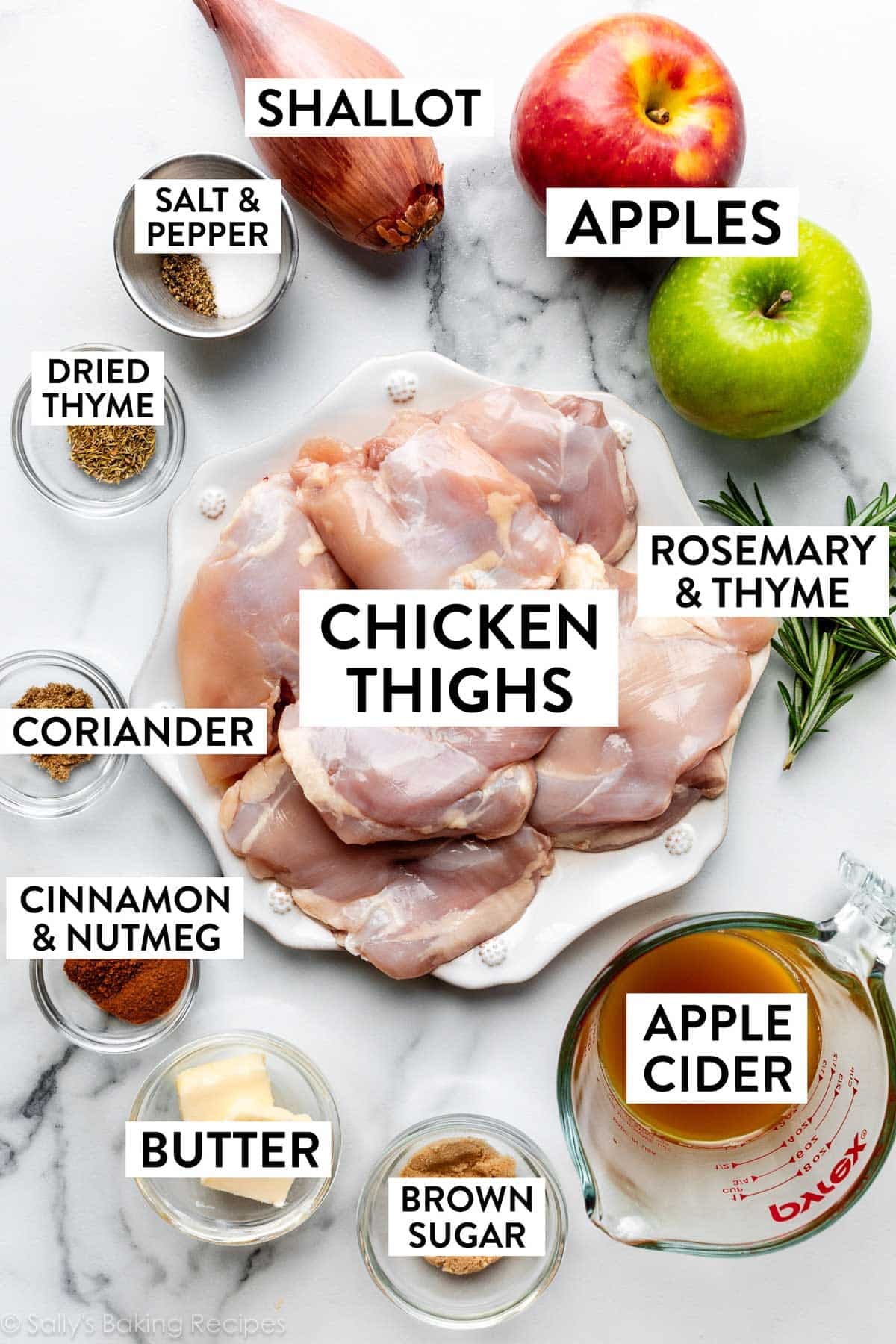 ingredients on marble counter including apples, chicken thighs on plate, brown sugar, apple cider, salt, pepper, and shallot.