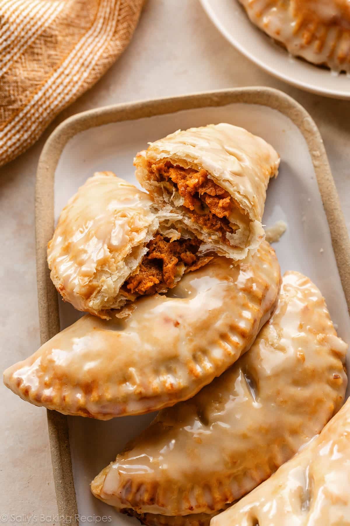 pumpkin hand pies with one cut in half on white serving tray.