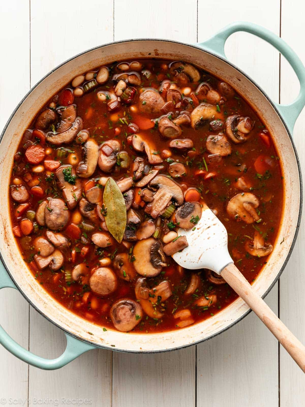 red wine and broth with mixed cooked vegetables and herbs in blue handled-skillet.