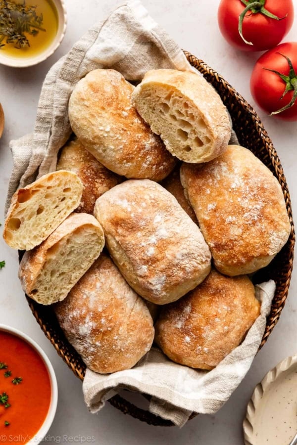 ciabatta rolls in basket with tomatoes, soup, and small bowl of dipping olive oil next to it.