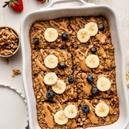 banana baked oatmeal in white casserole dish with blueberries and banana slices.