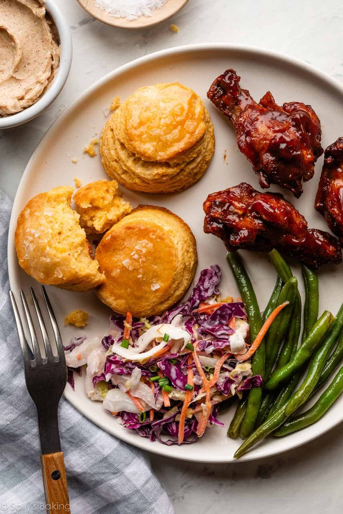 cornbread biscuits with coleslaw, beans, and bbq chicken on plate.