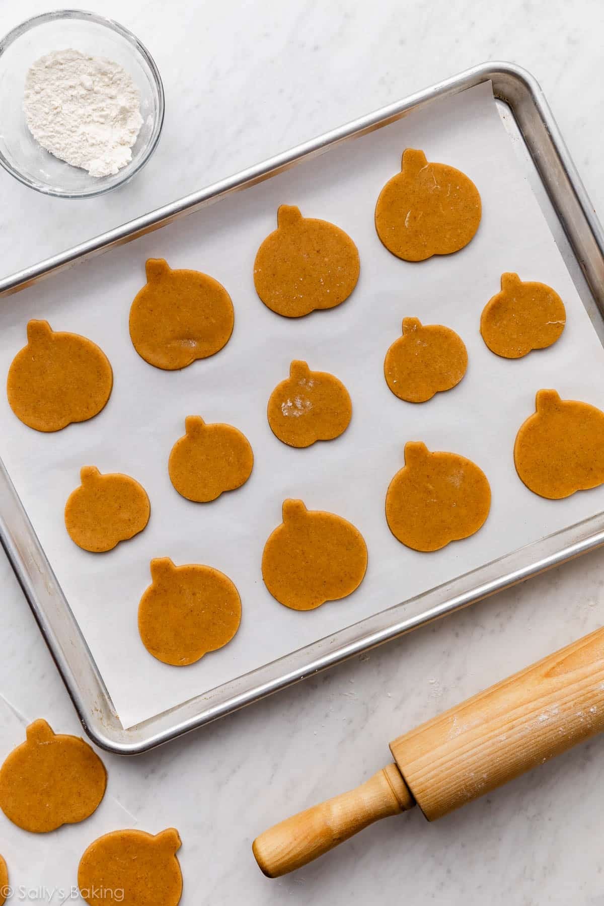 Pumpkin sugar cookies on a parchment-lined baking sheet before baking.